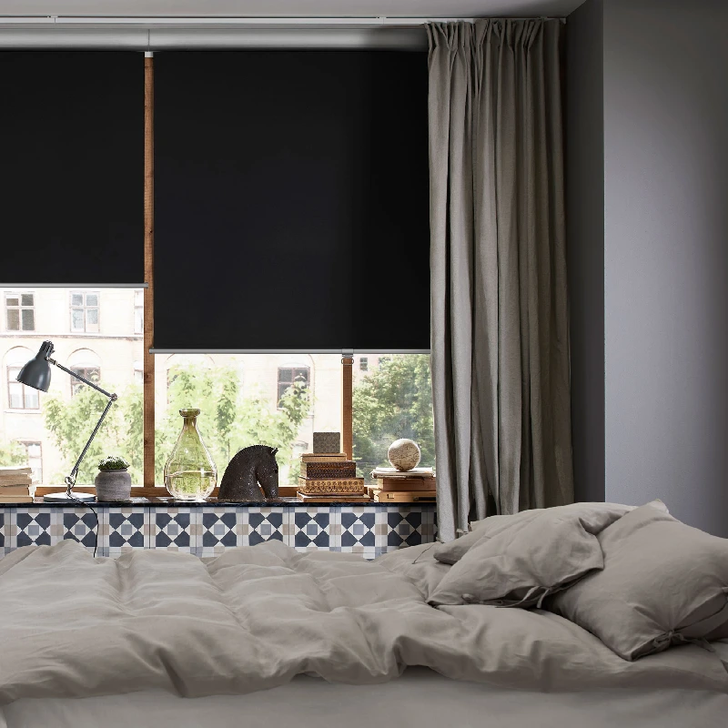 solid black blackout roller blind paired with grey curtains in a bedroom