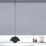 wide denim blue blackout roller blind fully covering a window behind a hanging pendant lamp